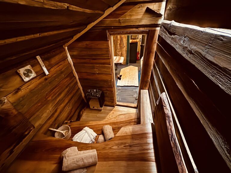 Pohled do vnitřního prostoru celodřevěné sauny s dřevěným vědrem, naběračkou a připravenými ručníky.